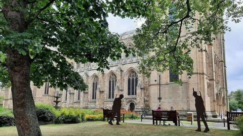 Ripon Cathedral - a Norman church surrounded by green gardens and soldier silhouettes. 