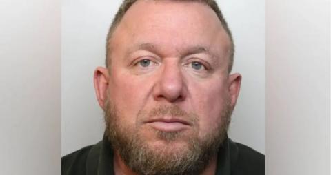A police custody head and shoulders mugshot of Mark Killick. He is looking straight at the camera and is wearing a dark shirt with a collar. He has short cropped ginger hair, and a mid-length beard and moustache.
