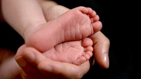 A baby's feet and legs being cradled by a left hand on a black blackground