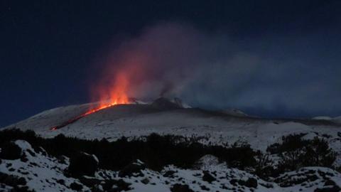 Orange lave spews from a crack in the snow-covered ground during the night