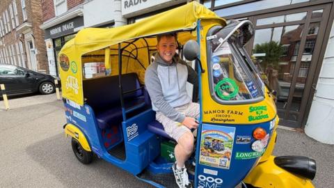A man in a yellow tuk tuk in a street