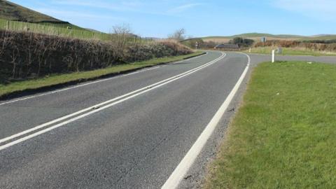 A long curving road through the south of Scotland countryside on a lovely blue-skied day