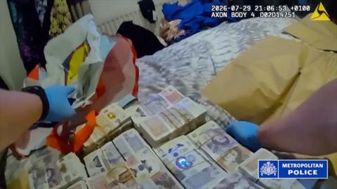 Bodycam footage showing gloved hands handling large bundles of cash on a bed, with Metropolitan Police watermark and timestamp.