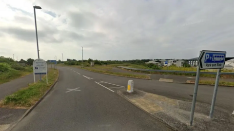 An image of a turning into a road. A sign on a traffic island is directing people to a park and ride. 