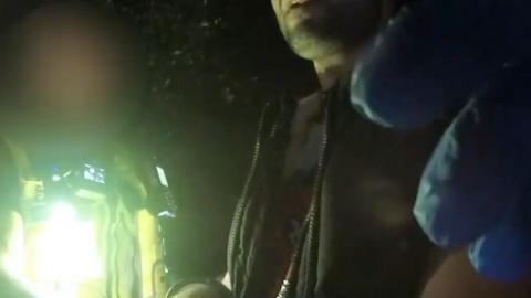 A police officer wearing a flashlight is stood next to a man in a black zip-up jacket