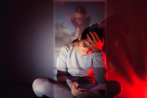 A girl sits in the shadow of a projected smartphone screen in a darkened room