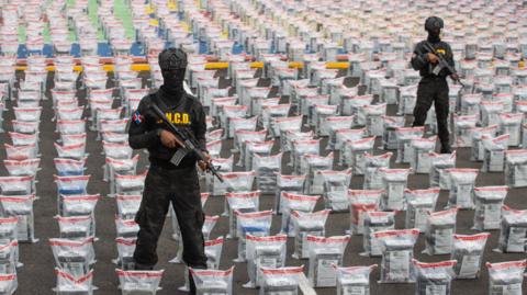 Police officers standing with guns in front of bags of cocaine