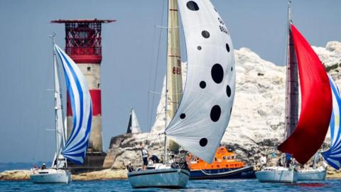 Sailing boats at The Needles, with colourful spinnakers and The Needles lighthouse behind.
