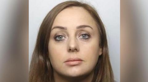 Mugshot of a woman with long straight brown hair. She has some eyeliner on and looks put-together. She has a neutral expression.