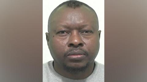 Mugshot of Ahmed. He has a short black goatee beard and shaved head with short black hair on top.