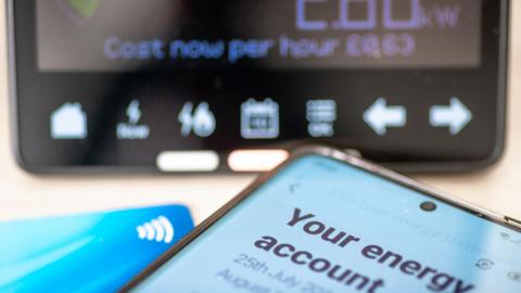 Energy account on phone next to bank card and in front of smart meter reading.