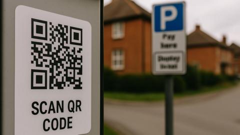 Stock image showing a QR code - black-and-white squares with a barcode-like appearance. A "Pay Here" sign can also be seen in the background as well as a row of houses.
