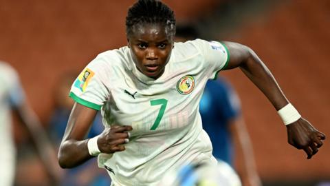 Mama Diop, wearing a white Senegal shirt, chases after the ball 