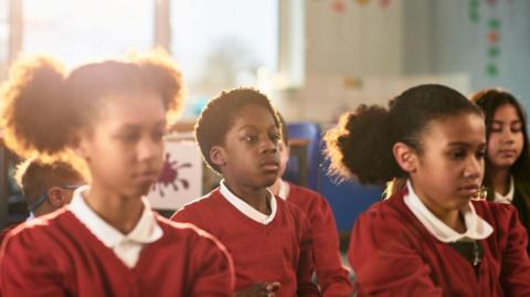 School children in red uniform preparing for relaxation session.