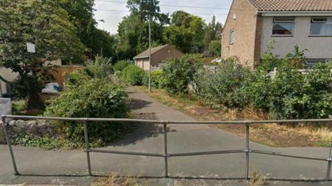 A Google Street View image shows a footpath leading away from St David's Road in Thornbury. A metal barrier sits between the pavement and the road at the end of the path. Bushes line the path.