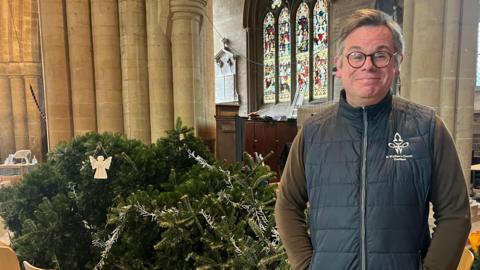 A bespectacled Father Stuart Cradduck standing in front of the toppled tree.