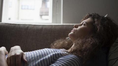 A young woman lying down on a sofa, looking into the distance