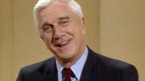 Leslie Neilsen smiling in medium close up against yellow background