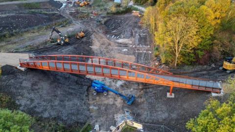 The bridge after being fixed into place. It is a browny red colour. There a number of telehandler vehicles nearby