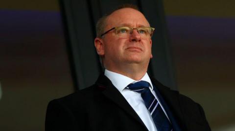 Mark Miles in a dark suit, white shirt, a navy blue West Bromwich Albion tie standing in the corporate box at The Hawthorns