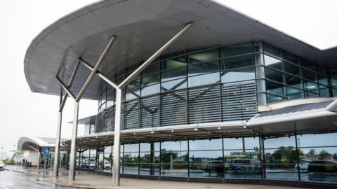 A picture of the entrance to Guernsey Airport. It has large glass-fronted windows and silver columns and roofing.