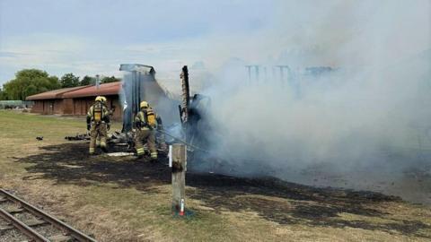 Firefighters next to a burnt static home with charred floor and smoke in the air