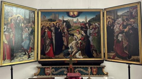 The triptych displayed above the almshouse altar. The side panels are turned inwards at 45 degrees. Each of the three panels is in a gold frame. 