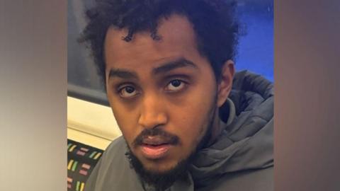 A close up of a young man sitting down in a London Underground carriage. 