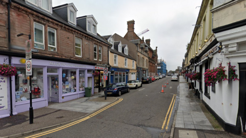 A screengrab of a narrow street with a number of brightly coloured shops visible.