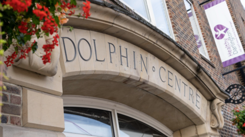 The exterior of the Dolphin Centre with flowers coming over the top left of the pale stone archway.