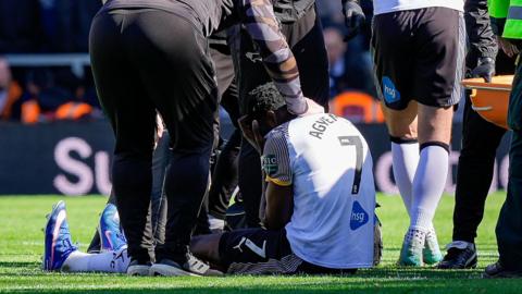 An image of Patrick Agyemang sitting on a football field surrounded by medics with his hands across his face in disappointment after picking up an injury