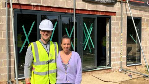 Tom Walsh and Elisa Sonaglioni stand in front of their home which is supported by scaffolding. 