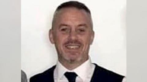 Phillip Thompson with very short dark hair, wearing a white shirt, dark tie and dark waistcoat, smiling to camera