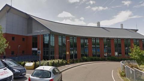 Loddon Valley Police Station - a red brick building that curves with the curve in the road. It has lots of windows. There are two cars and a van parked up to the right in the foreground.