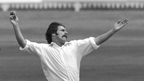 Peter Lee with his left arm raised is about to bowl a ball with his right hand and his shirt sleeves rolled up in a black-and-white image 