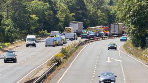 Police cars and fire engines at the scene of a crash on the A38 near Buckfastleigh in Devon. Several other cars, lorries and vans are also at the scene.