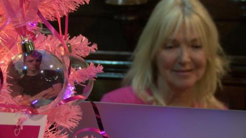 Lisa Wilson smiles at her computer. In the foreground a bauble of her son Tom hangs off a pink Christmas tree.