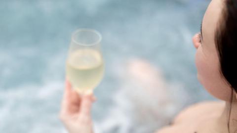 A woman in a hot tub drinking prosecco