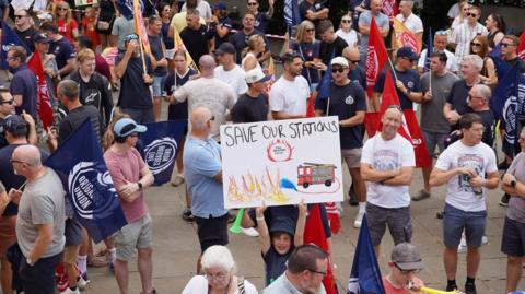 A number of people at a demonstration organised by the Fire Brigades Union on Tuesday, August 4, outside Maidstone County Hall. A child is holding up a sign which says 'Save our Stations'. A number of people are holding flags.