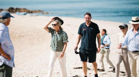 A picture of Sophie, Duchess of Edinburgh, meeting islanders. She is wearing a green and yellow short-sleeved blouse and she is wearing sunglasses.