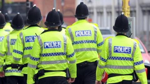 A group of police officers walking away from the camera wearing high-visibility jackets. 