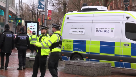 Police officers stood outside vans in Reading town centre with a van that says "facial recognition currently in use" and Thames Valley Police's logo next to it.