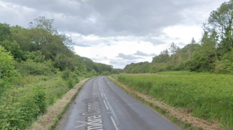 A Google street view of Ranmore Common Road, showing a rural road with fields and trees on either side.