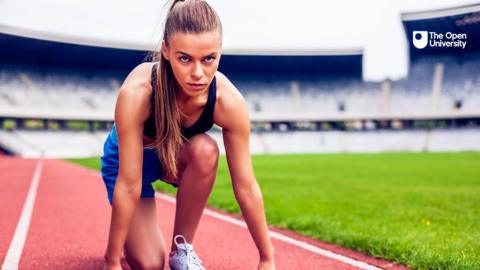 A female runner crouches down on a track staring straight ahead 