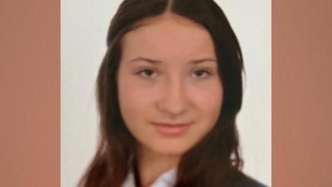 Scarlett has long brown hair and is looking at the camera with a slight smile. She is wearing a white shirt, a navy and white striped tie and a navy blazer.