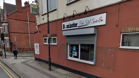 A red and white building on the corner of a street with roller shutters and a sign that reads: Doncaster Park Social Sports Bar