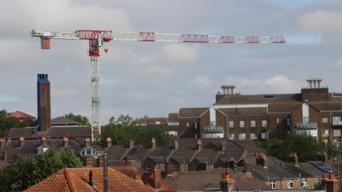 A large red and white crane rises high above the brown brick buildings below.