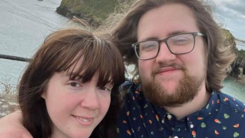Ameila and Lewis Relfe smiling. Sea water can be seen behind them.
