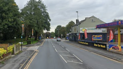 Image shows Oldham Road in Royton. There is a car wash on one side and a small park on the other. 