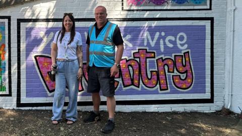 A woman and a man standing by a large mural